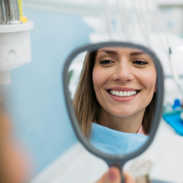 woman looking at smile in mirror at dentist's office